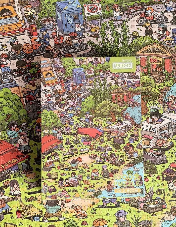 Completed puzzle laid flat with box placed on top, highlighting the crowded, humorous campsite artwork.