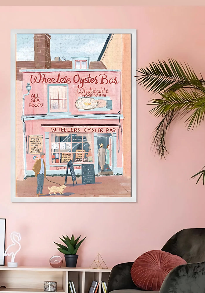 Framed completed puzzle on pink wall above lounge – seaside town puzzle.