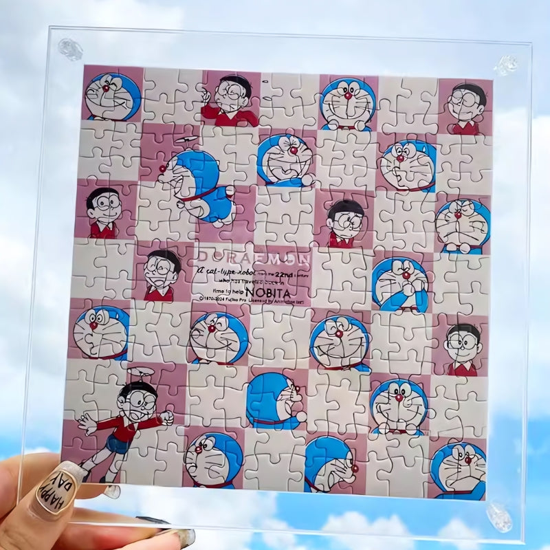 Completed Doraemon checkerboard mini puzzle held against a bright blue sky, displayed inside a clear acrylic frame with visib