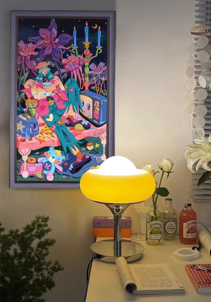 Framed Night Garden puzzle displayed on a wall above a desk with a glowing lamp and books.