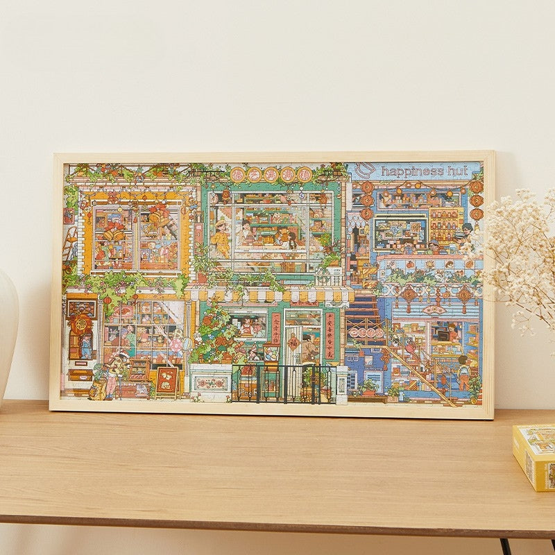 Framed completed Happiness Hut Keytime jigsaw puzzle on wooden sideboard, featuring colourful houses and shops.
