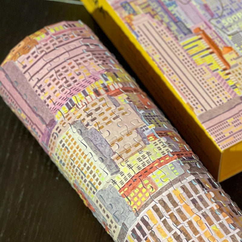 Rolled-up section of completed Fantasy Manhattan puzzle beside its yellow PERMA box.