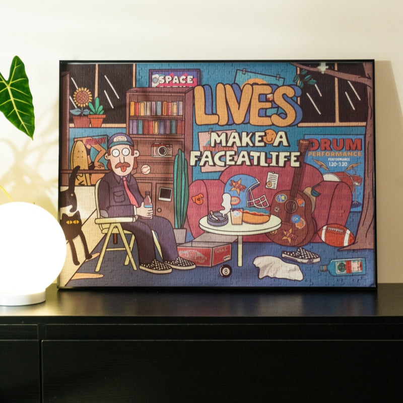 Wide shot of the framed Make a Face At Life puzzle displayed on a shelf with a glowing lamp and plant beside it.