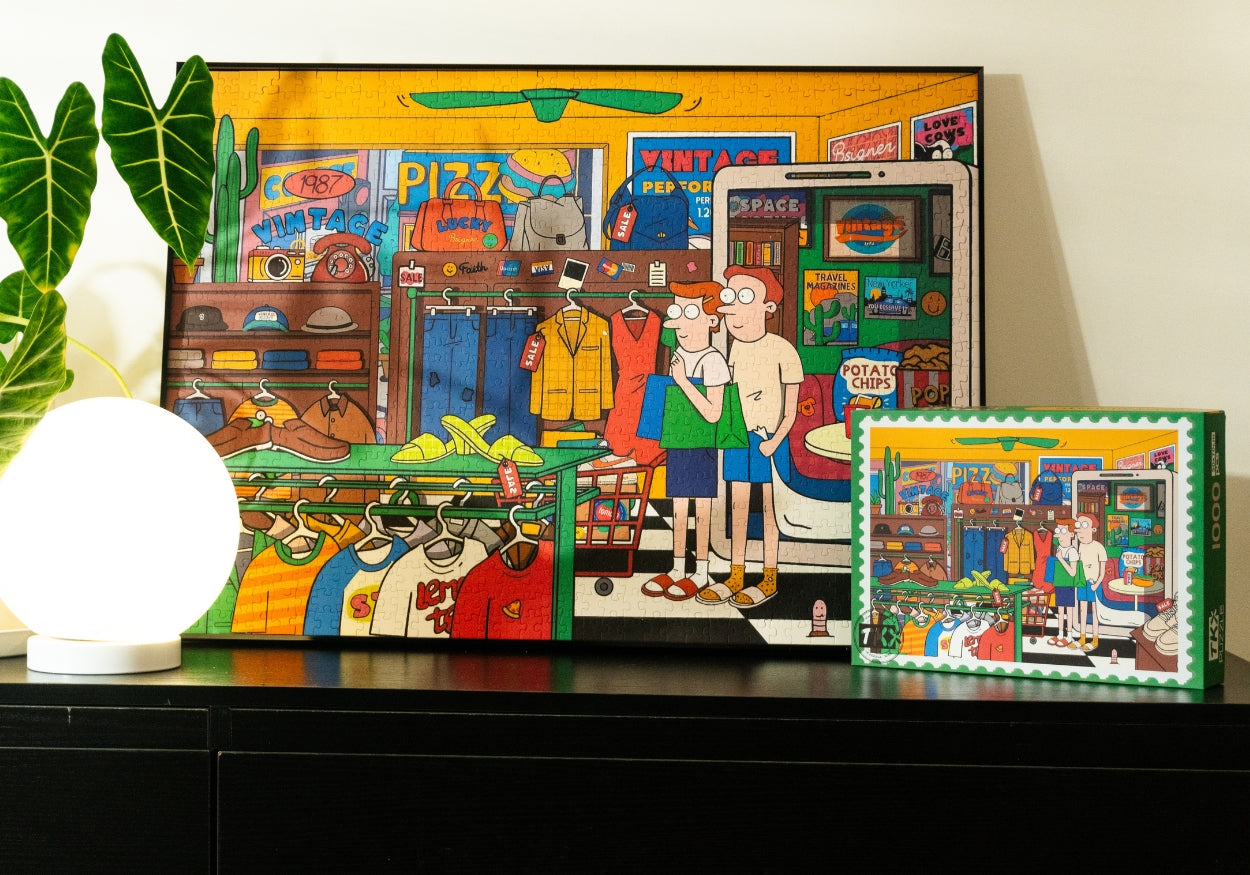 A framed completed puzzle displayed on a shelf next to a green potted plant and a white round lamp. The puzzle depicts the detailed cartoon shopping scene with the couple browsing clothes, various shoes on display, and colorful signs and items filling the background.