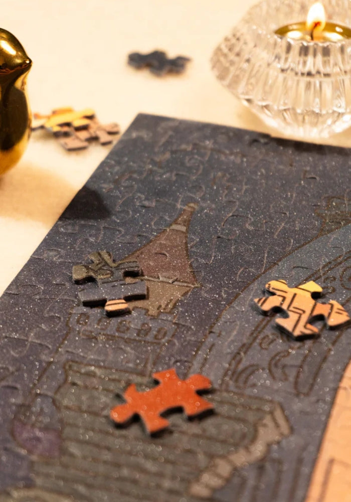 Puzzle corner with loose pieces and a candle, highlighting dark blue night sky and puzzle glitter texture