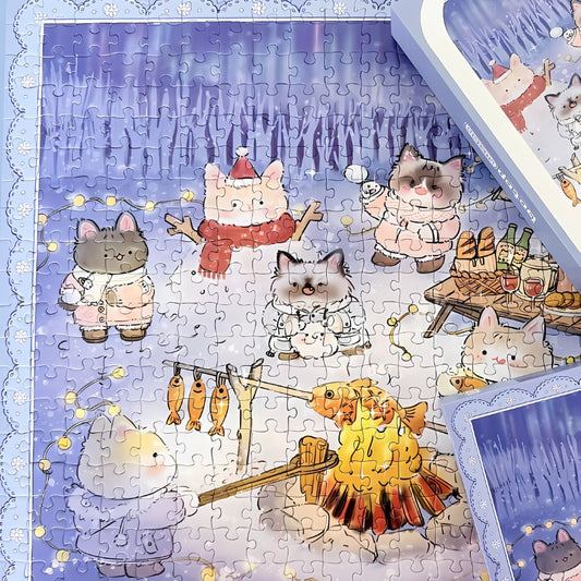 Assembled Aurora puzzle with the box, showing the snowy cat campsite and festive details.