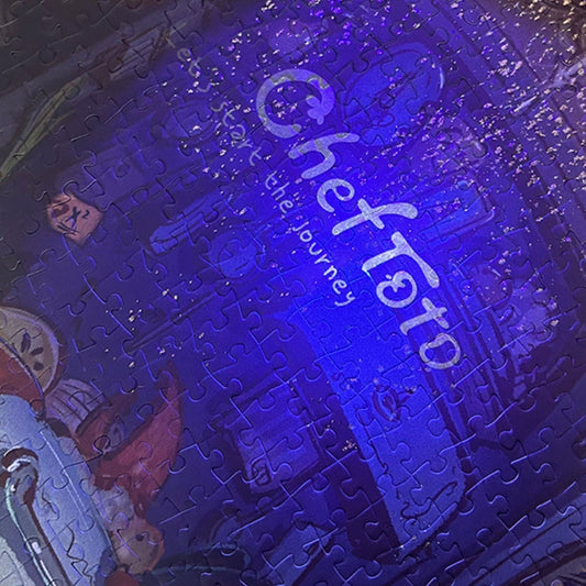 Close-up of puzzle under blacklight showing ‘Chef Toto’ logo glowing with glitter and hidden details