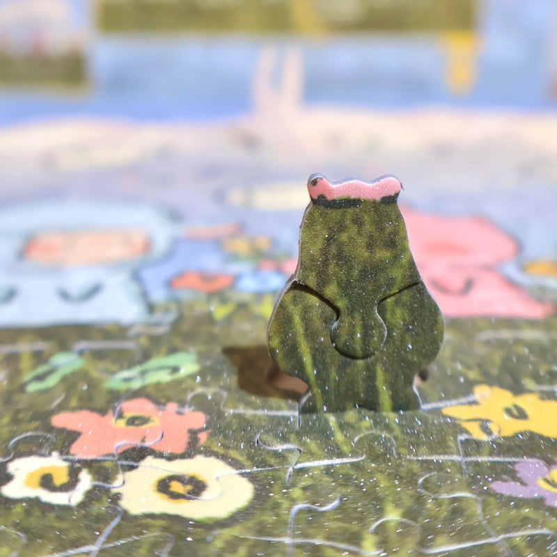 lose-up of green puzzle piece shaped like a frog standing upright on completed puzzle background.