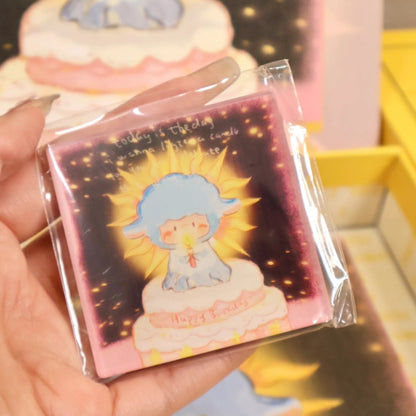 Close-up of a hand holding the fridge magnet featuring the ‘Let the Candles Burn’ cake-top character with glowing candle and golden rays.