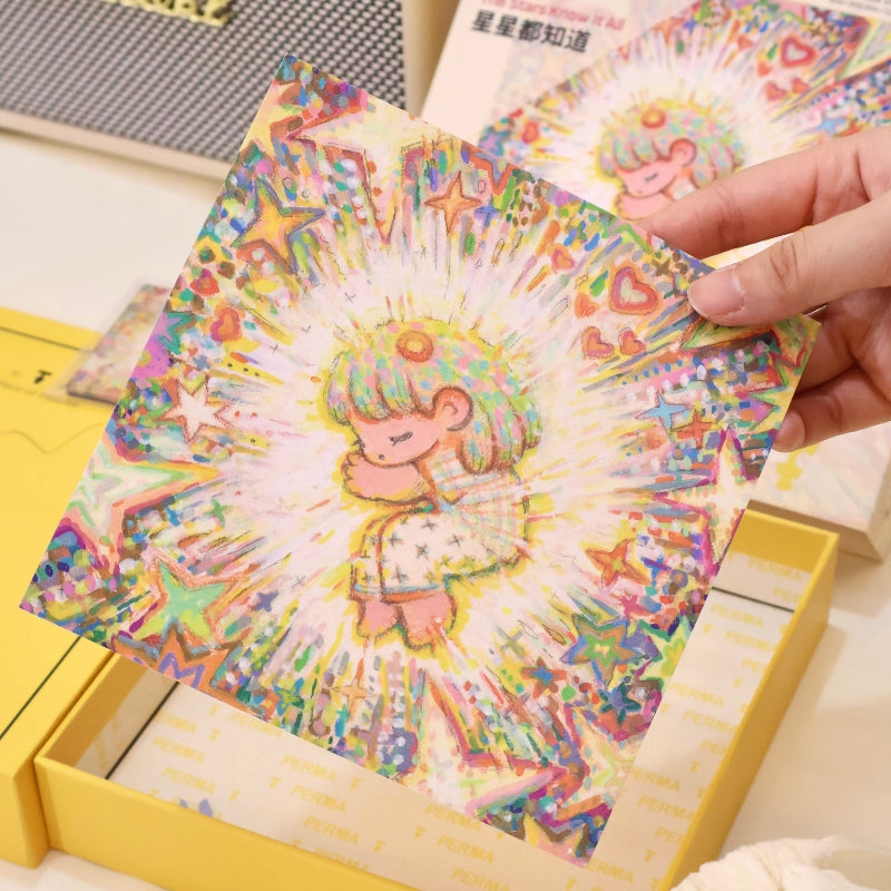 Person holding a square postcard-style art print of the puzzle illustration above the yellow puzzle box.
