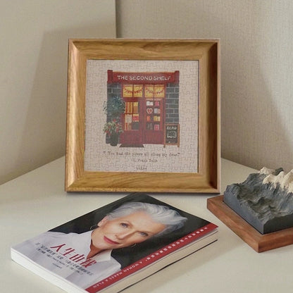 Completed and framed Pin Pin The Second Shelf mini puzzle displayed on a desk beside books and decor.